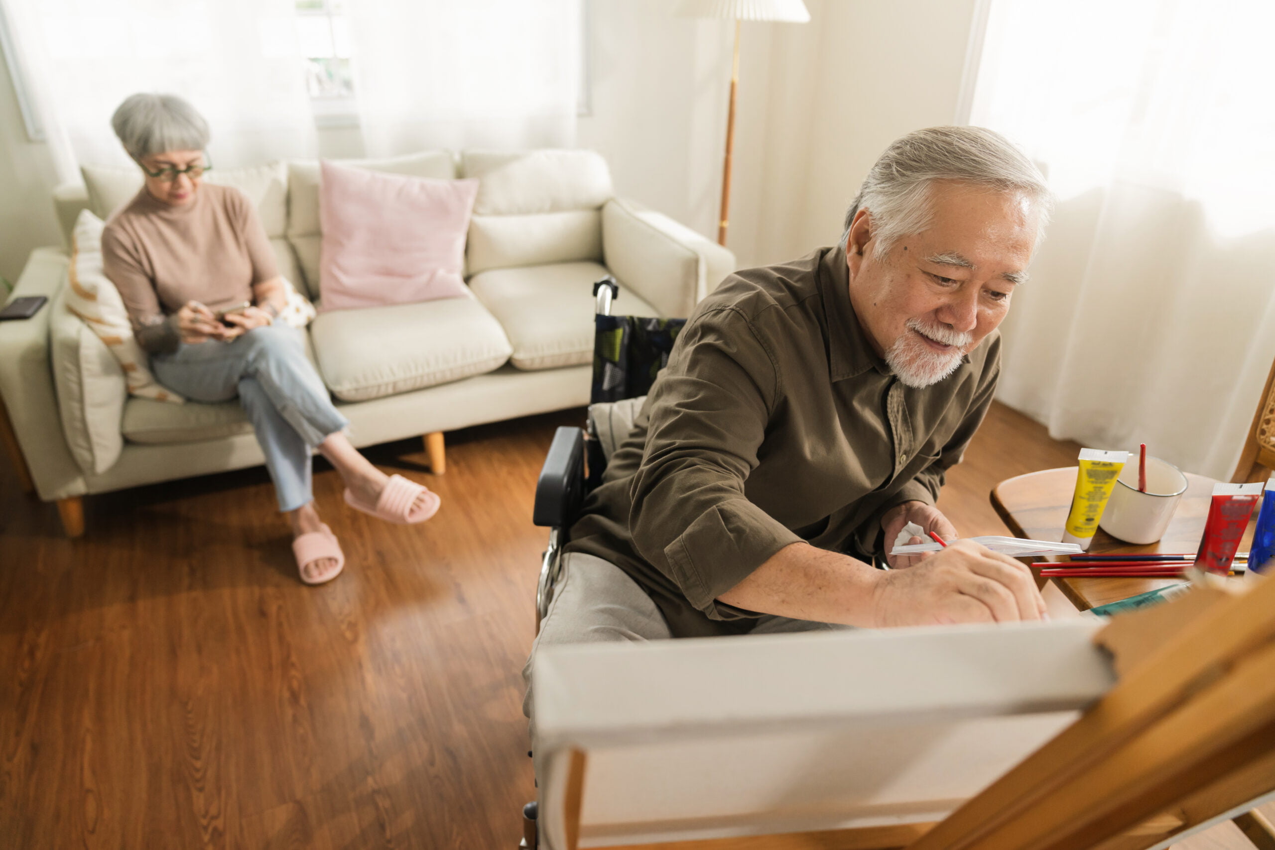 velho homem asiático sênior usando arteterapia enquanto suas pernas estão feridas em casa, homem mais velho asiático gasta se recuperando de sua perna está melhorando com a pintura de tela na sala de estar com sua esposa em casa